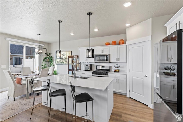 kitchen featuring pendant lighting, sink, light wood-type flooring, white cabinetry, and stainless steel appliances