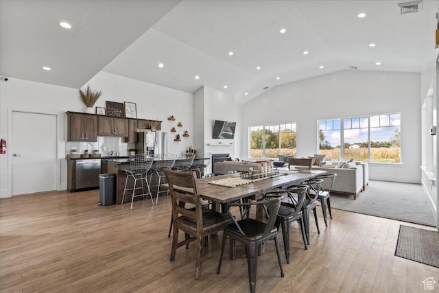 dining area with high vaulted ceiling and light hardwood / wood-style floors