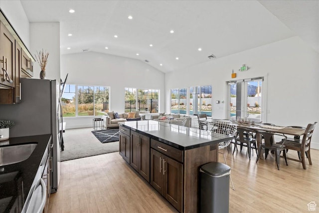 kitchen with dark brown cabinetry, a center island, lofted ceiling, and light wood-type flooring