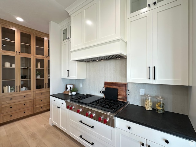 kitchen featuring decorative backsplash, custom exhaust hood, stainless steel gas cooktop, white cabinets, and light hardwood / wood-style floors