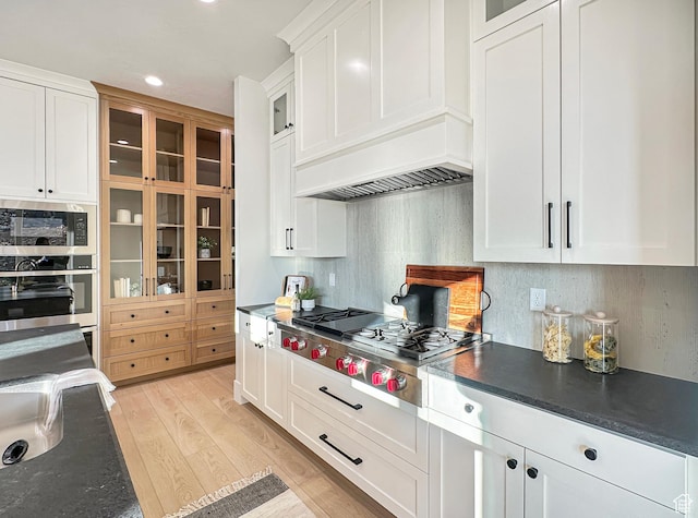 kitchen featuring backsplash, premium range hood, light hardwood / wood-style floors, white cabinets, and appliances with stainless steel finishes