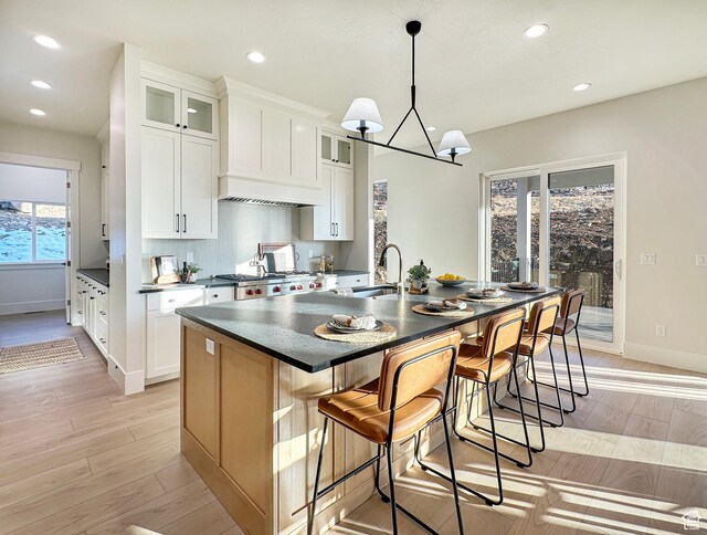 kitchen with white cabinets, a center island with sink, sink, and light hardwood / wood-style flooring