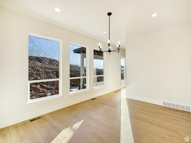 unfurnished dining area featuring a wealth of natural light, light hardwood / wood-style floors, and an inviting chandelier