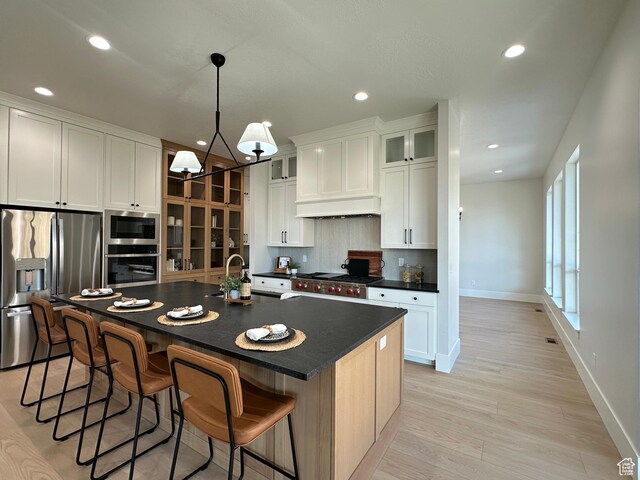 kitchen with sink, hanging light fixtures, stainless steel appliances, a kitchen island with sink, and white cabinets