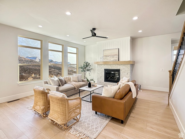 living room featuring a fireplace, light hardwood / wood-style floors, and ceiling fan