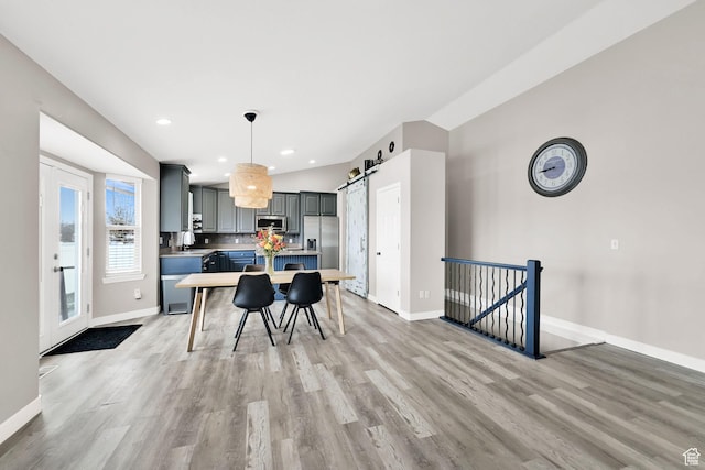 kitchen with gray cabinets, a barn door, stainless steel appliances, baseboards, and light wood-style floors