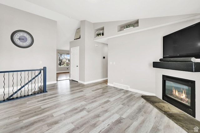 unfurnished living room with high vaulted ceiling, visible vents, baseboards, wood finished floors, and a glass covered fireplace