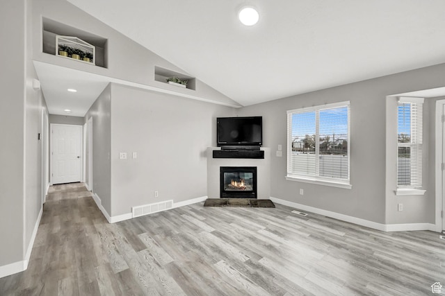 unfurnished living room featuring baseboards, visible vents, light wood-style flooring, and a glass covered fireplace