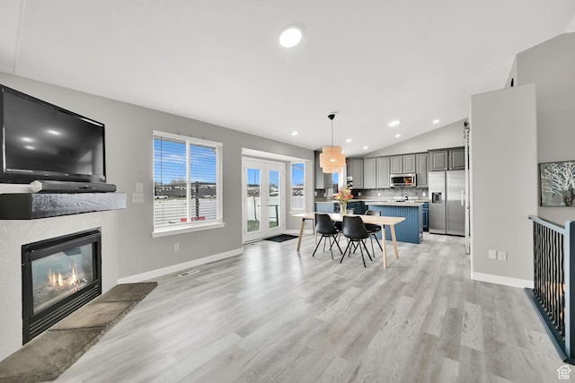 dining area with vaulted ceiling, a glass covered fireplace, light wood-type flooring, baseboards, and recessed lighting