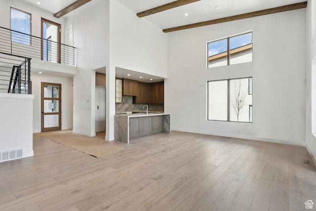 5758 Cobalt Cir Unit 12, Park City, UT 84098 - unfurnished living room featuring a towering ceiling, baseboards, light wood finished floors, beam ceiling, and a sink
