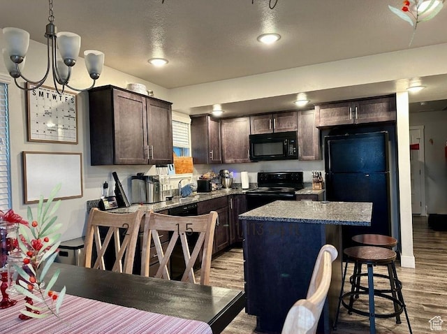 kitchen with an inviting chandelier, black appliances, hanging light fixtures, light hardwood / wood-style flooring, and light stone countertops