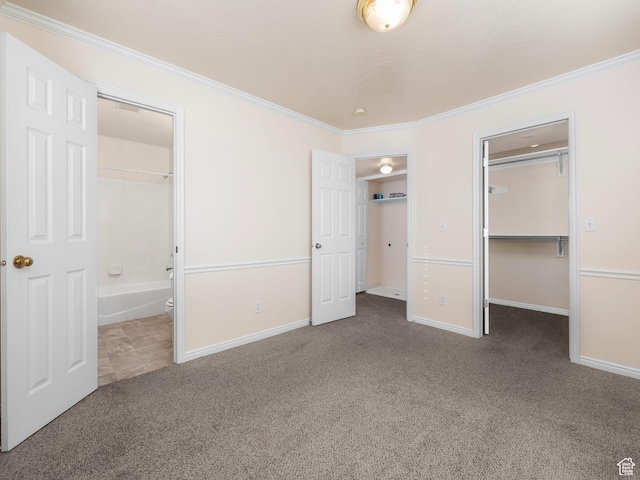 unfurnished bedroom with ornamental molding, baseboards, a walk in closet, and carpet