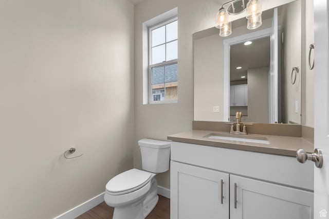 half bath featuring vanity, toilet, wood finished floors, and baseboards