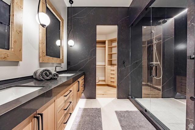 bathroom with a shower stall, double vanity, a sink, and a walk in closet