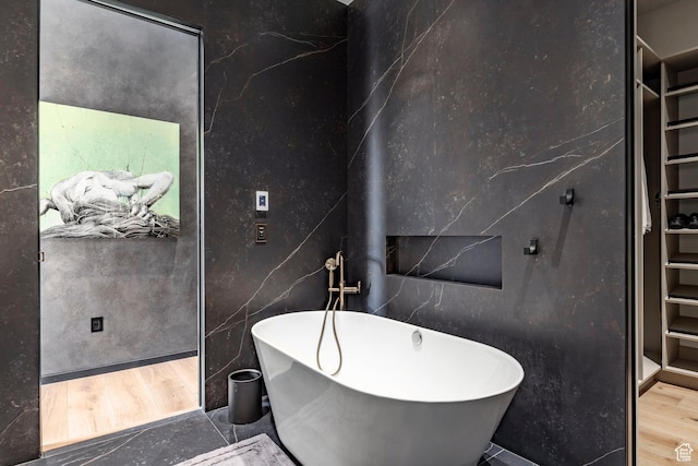 bathroom with a spacious closet, a freestanding tub, and wood finished floors