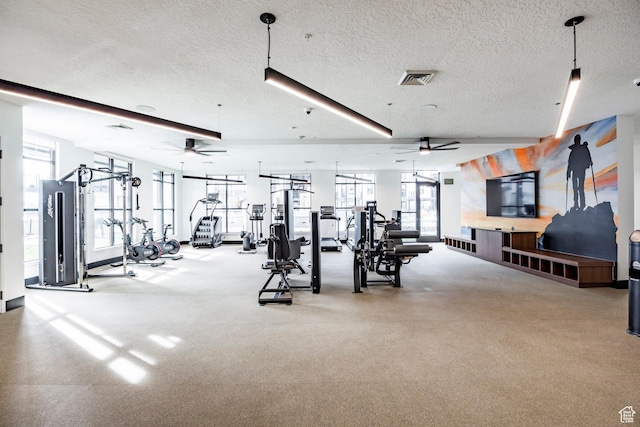 gym featuring ceiling fan, a wealth of natural light, and a textured ceiling