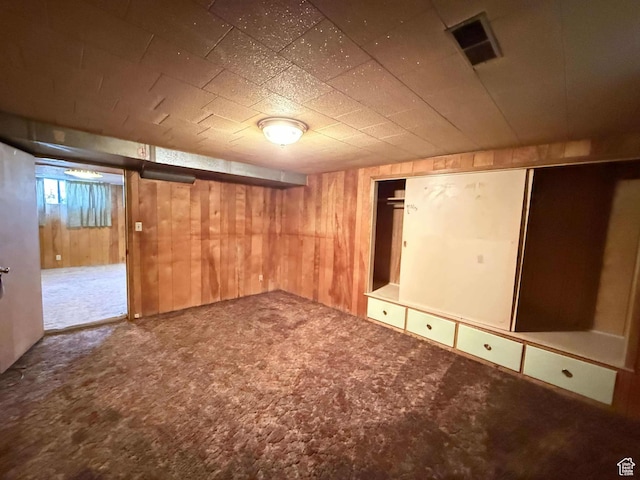 finished basement with carpet, visible vents, and wooden walls