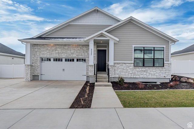 craftsman house with driveway, fence, an attached garage, and stone siding