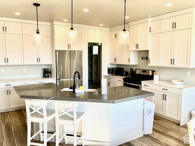 3260 Retreat Dr S, Hurricane, UT 84737 - kitchen with white cabinetry, a center island with sink, wood-type flooring, and appliances with stainless steel finishes