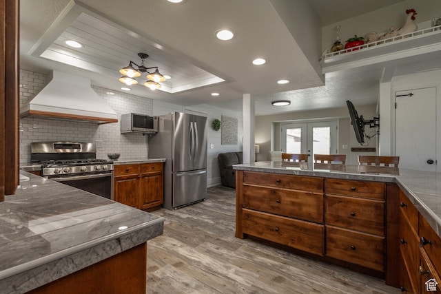 kitchen with french doors, premium range hood, stainless steel appliances, a raised ceiling, and wood-type flooring
