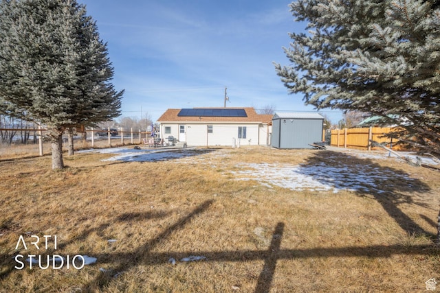 back of house with solar panels, a storage shed, and a yard