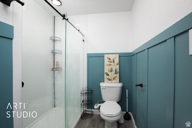 bathroom with toilet, a shower with shower door, and hardwood / wood-style flooring