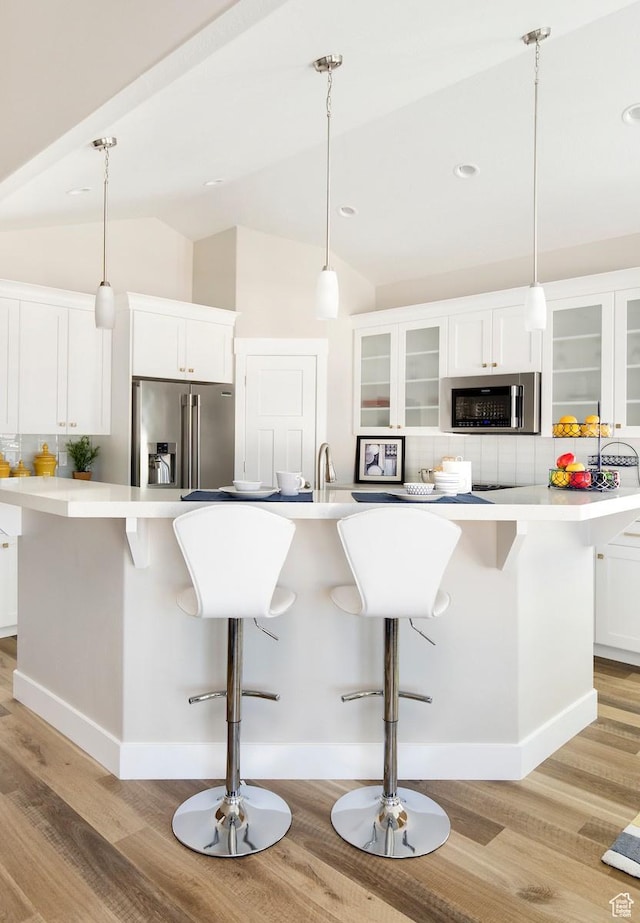 kitchen featuring white cabinets, a large island with sink, stainless steel appliances, and vaulted ceiling