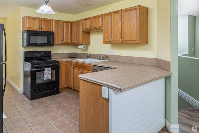 kitchen featuring kitchen peninsula, sink, black appliances, pendant lighting, and tile countertops