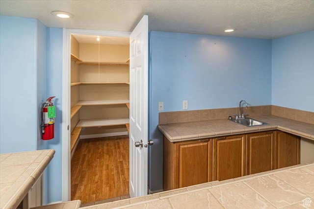 kitchen with tile countertops, sink, hardwood / wood-style floors, and a textured ceiling