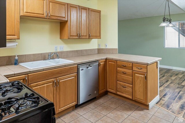 kitchen featuring stainless steel dishwasher, sink, pendant lighting, tile countertops, and black range