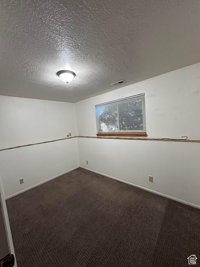 unfurnished room featuring dark carpet and a textured ceiling
