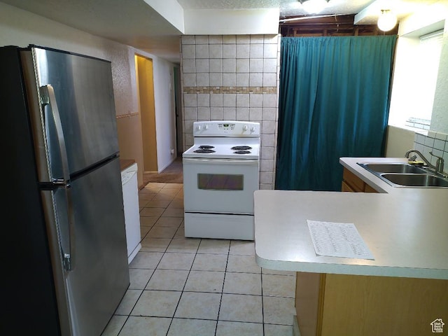 kitchen featuring stainless steel refrigerator, sink, white electric range, light tile patterned flooring, and tile walls