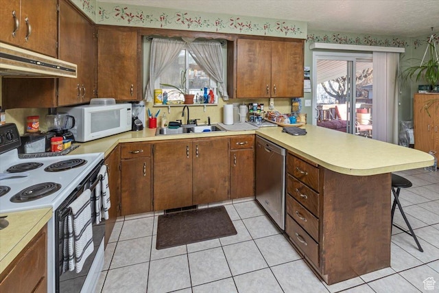kitchen with a healthy amount of sunlight, white appliances, kitchen peninsula, and sink