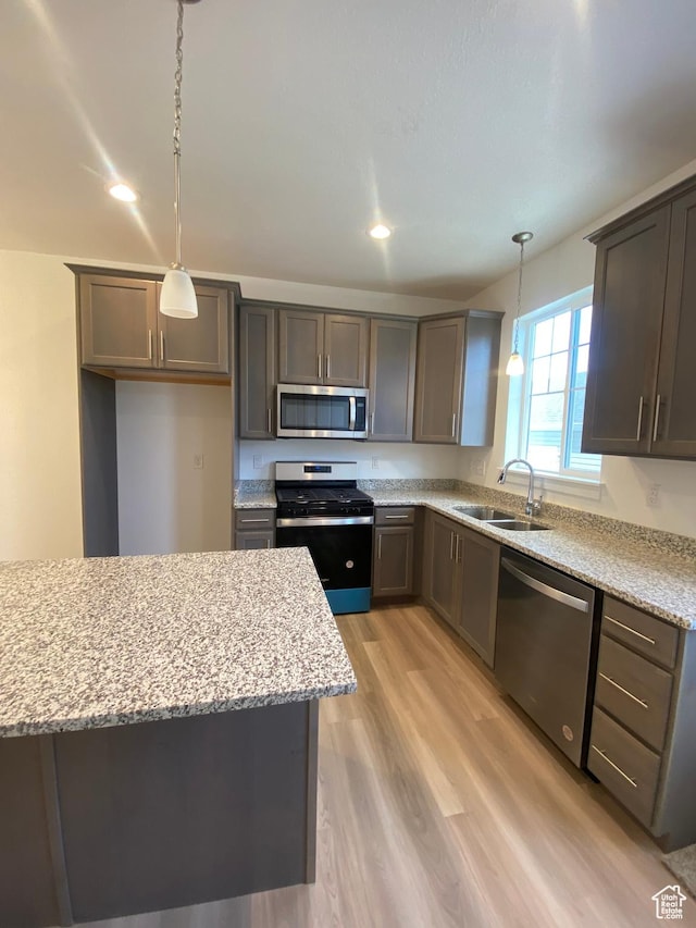 kitchen featuring sink, light hardwood / wood-style flooring, light stone countertops, decorative light fixtures, and stainless steel appliances