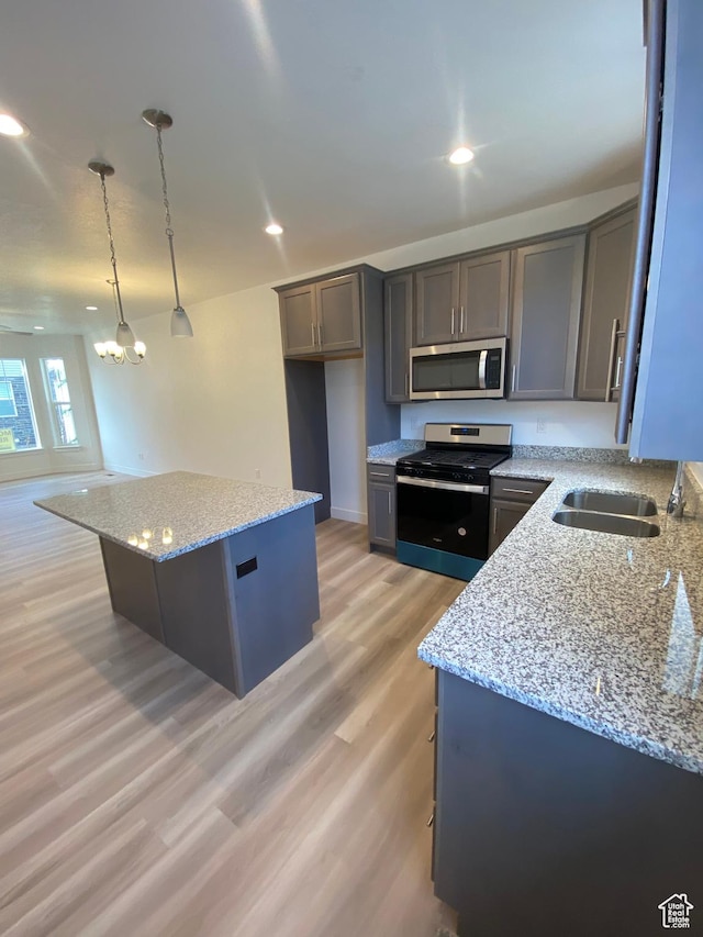kitchen with a center island, hanging light fixtures, light stone countertops, light wood-type flooring, and stainless steel appliances