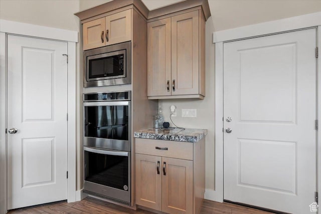 kitchen featuring dark hardwood / wood-style flooring, light brown cabinetry, dark stone countertops, and appliances with stainless steel finishes