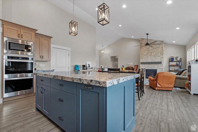 kitchen featuring stainless steel appliances, ceiling fan, light hardwood / wood-style floors, a stone fireplace, and hanging light fixtures