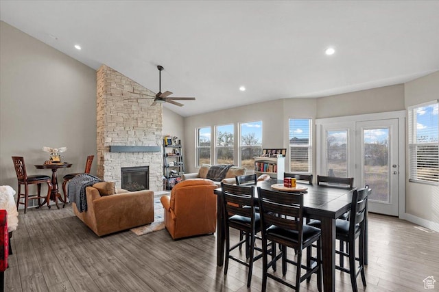 dining space with a healthy amount of sunlight, a stone fireplace, light wood-type flooring, and vaulted ceiling
