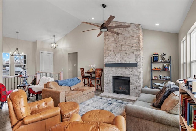 living room featuring hardwood / wood-style flooring, ceiling fan with notable chandelier, a stone fireplace, and high vaulted ceiling