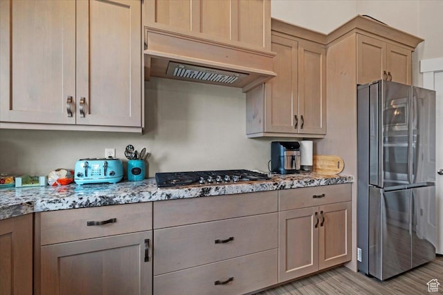 kitchen featuring light brown cabinets, light stone counters, light hardwood / wood-style flooring, premium range hood, and appliances with stainless steel finishes