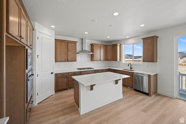 kitchen featuring sink, wall chimney exhaust hood, light hardwood / wood-style flooring, a kitchen island, and appliances with stainless steel finishes