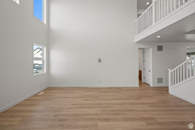 unfurnished living room featuring a high ceiling and light hardwood / wood-style flooring