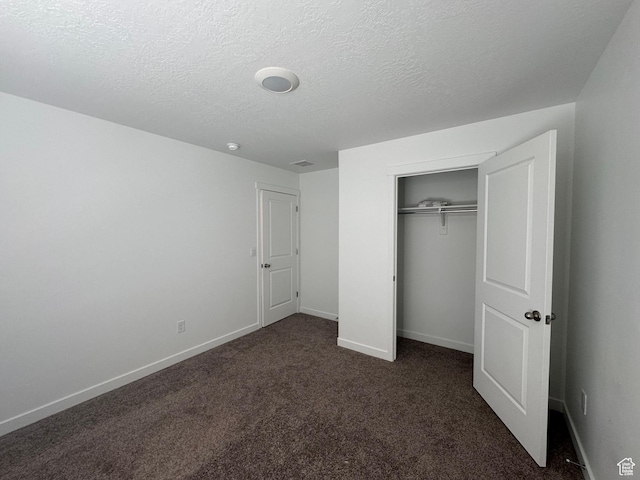unfurnished bedroom featuring a closet, dark carpet, and a textured ceiling