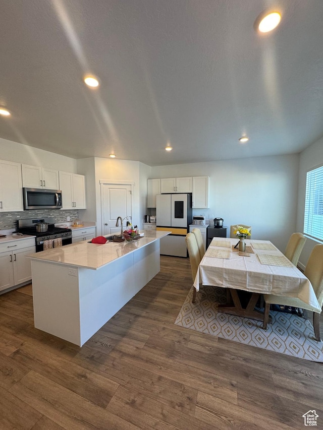 kitchen with white cabinetry, stainless steel appliances, dark hardwood / wood-style floors, backsplash, and a center island with sink