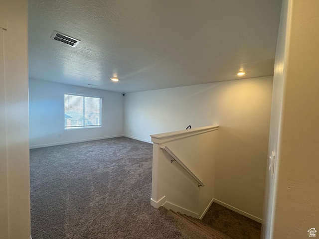 empty room with dark colored carpet and a textured ceiling