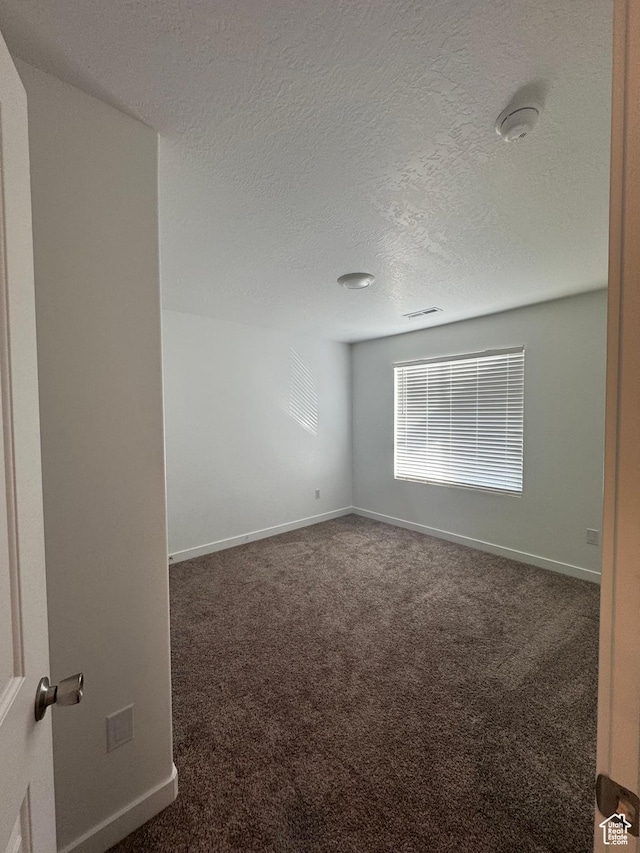empty room with a textured ceiling and dark carpet