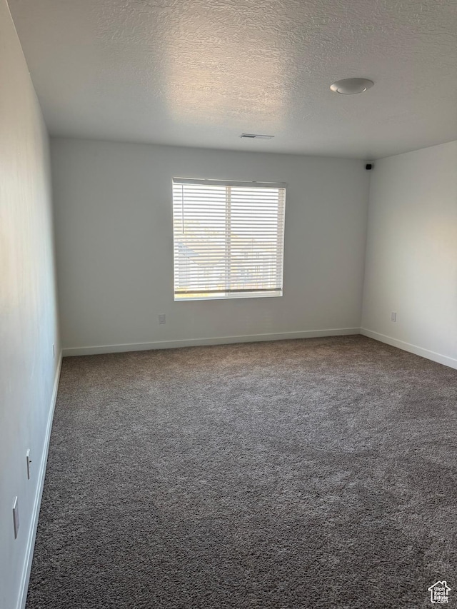 spare room featuring dark carpet and a textured ceiling