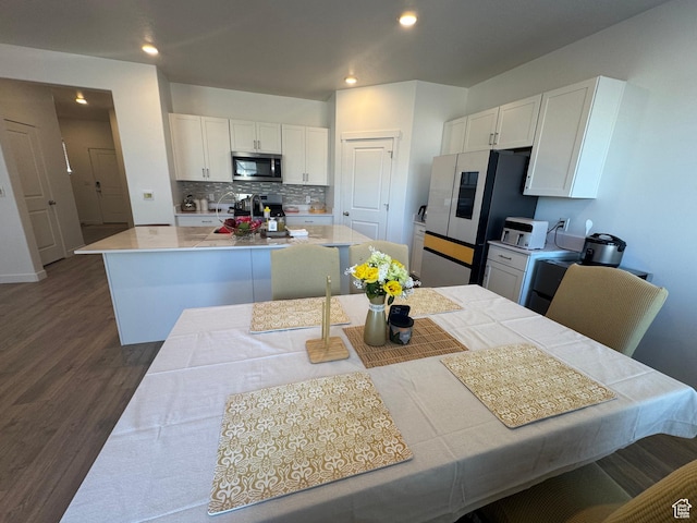 kitchen with dark wood-type flooring, stainless steel appliances, a kitchen island, decorative backsplash, and white cabinets