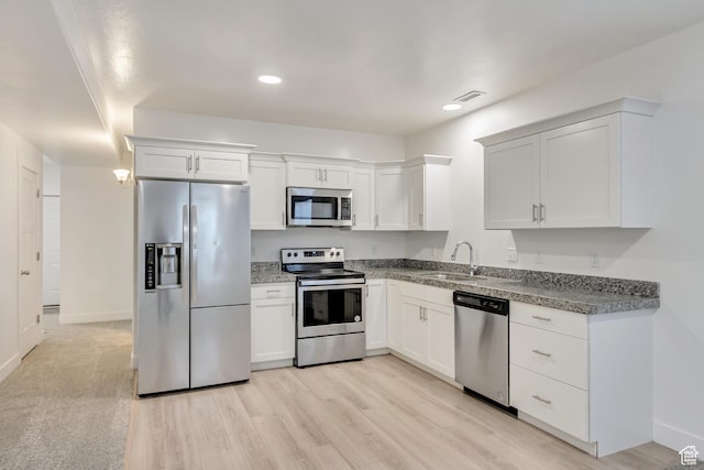 kitchen with appliances with stainless steel finishes, light wood-type flooring, white cabinetry, and sink