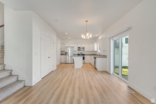 kitchen featuring appliances with stainless steel finishes, decorative light fixtures, light hardwood / wood-style flooring, a center island, and white cabinetry